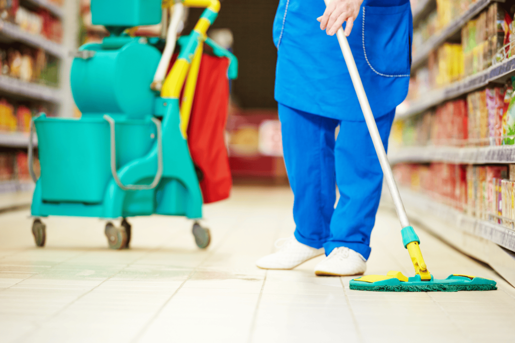 Een schoonmaker dweilt de vloer van een supermarkt met professionele schoonmaakapparatuur.