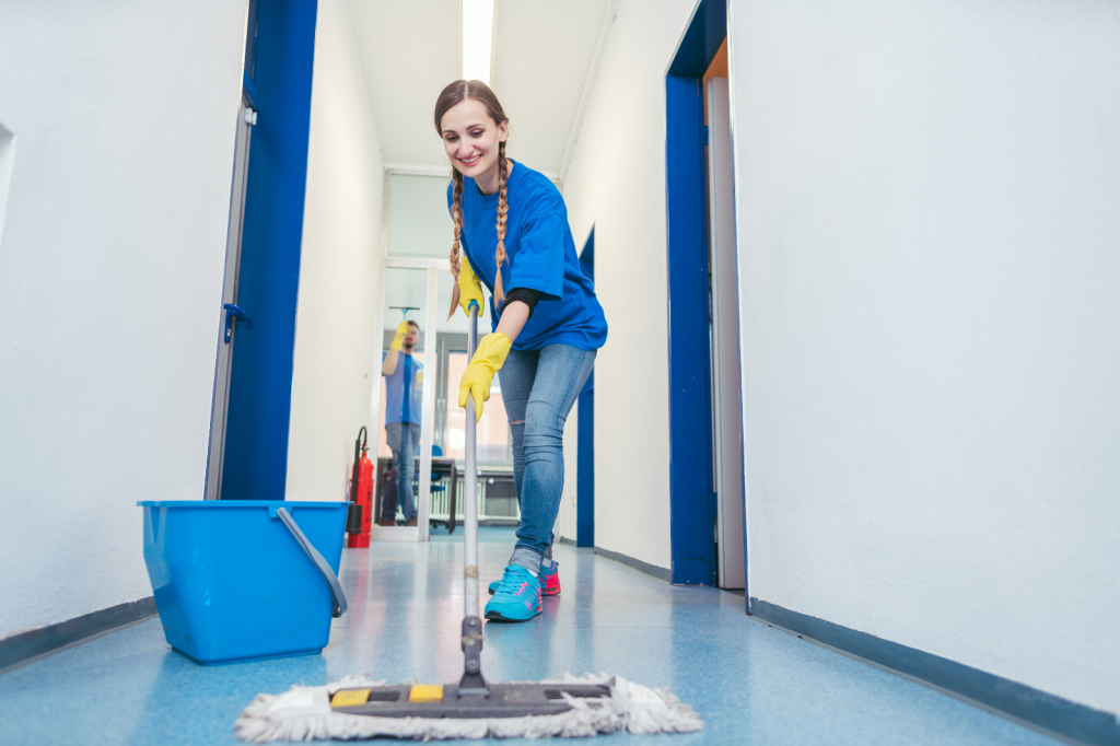 Medewerker reinigt een vloer in een bedrijfsruimte met een mop en emmer.